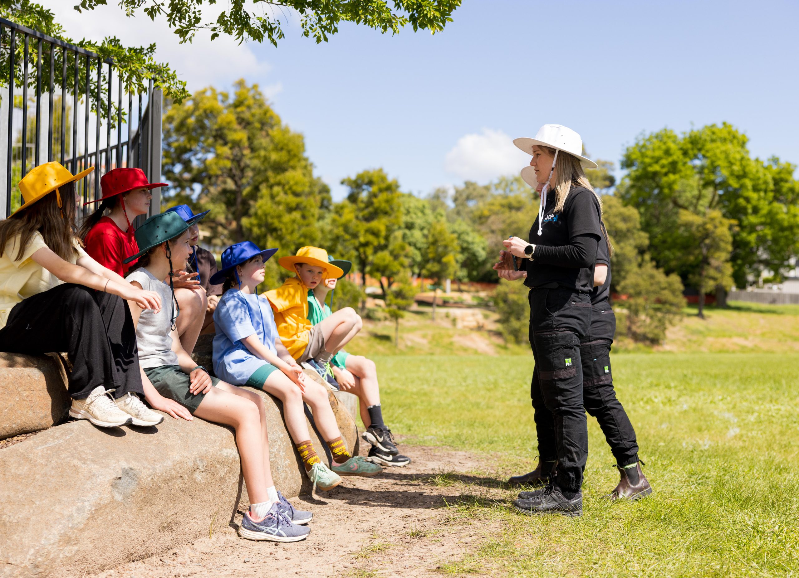 Children in colourful hats with a Kaleido Camps team member outdoors.