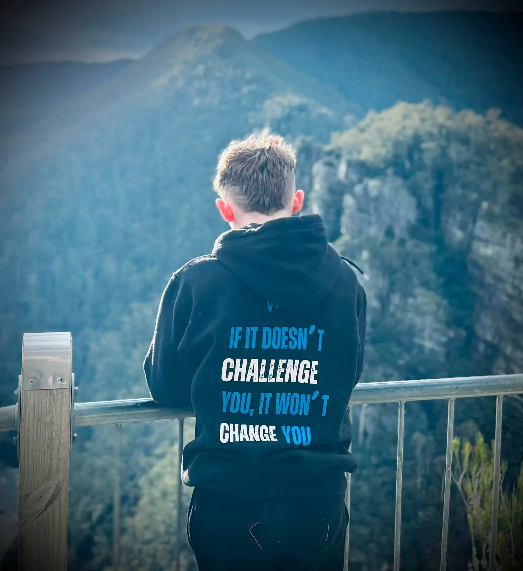 A young person wearing a JCP hoodie looks out across a mountain landscape.