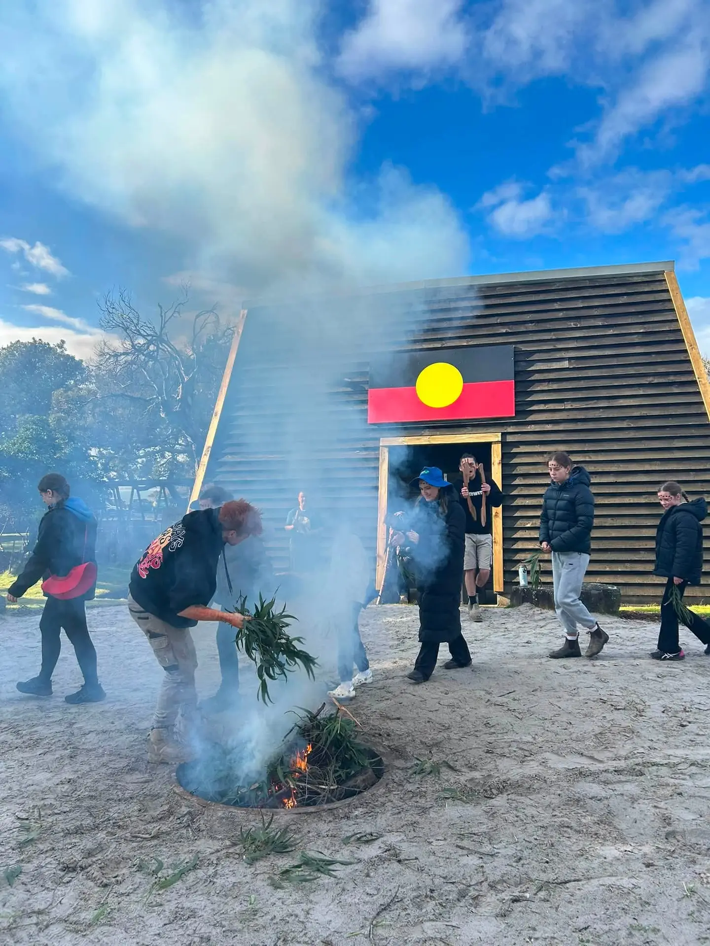 Kaleido camp group outdoors beside a smoking fire pit and a timber building.